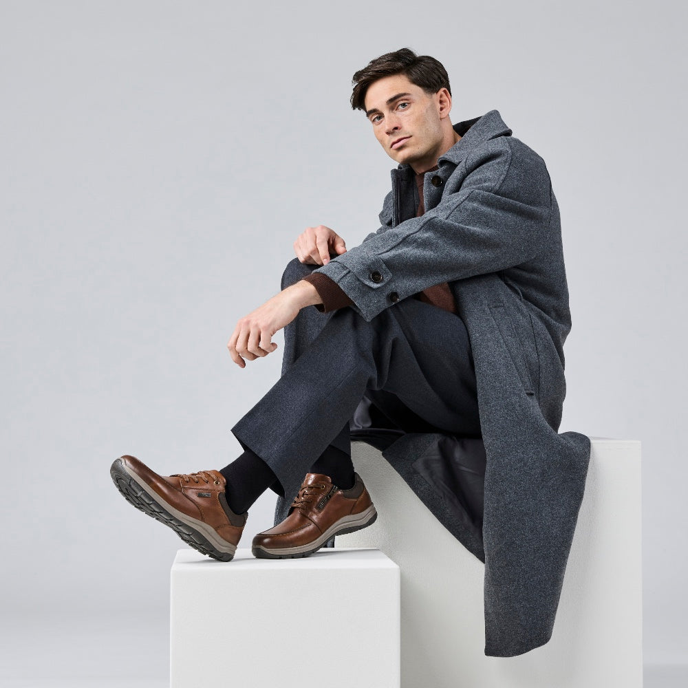 Image of a man sitting against a white background wearing brown Rieker trainers