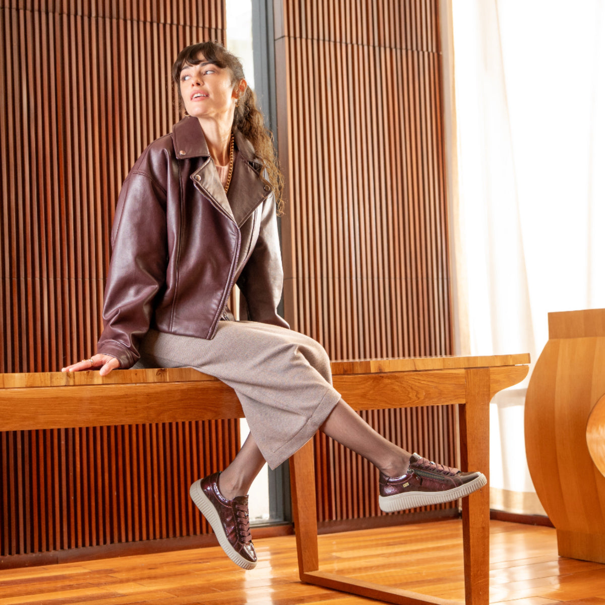 A woman sits on a wooden table, she is wearing brown rieker trainers