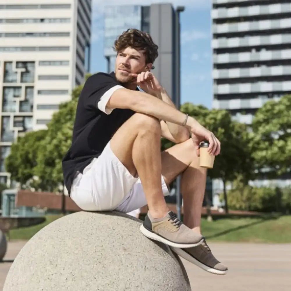 Image of a man standing against a brown and blue background wearing brown Rieker boots