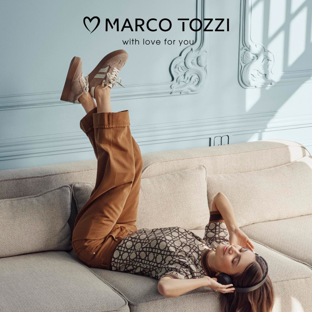 A woman lies ona sofa wearing headphones and marco tozzi sneakers
