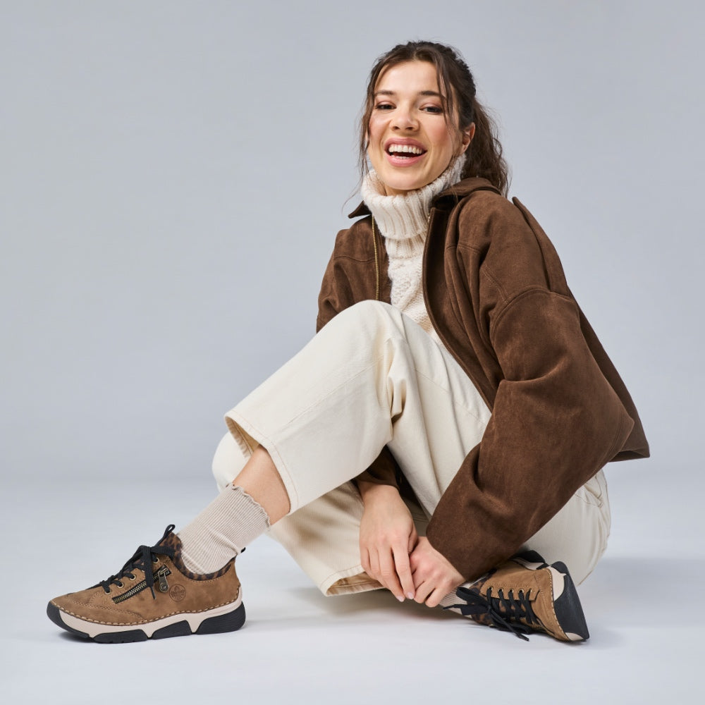 woman sitting cross legged on the floor wearing brown riekr trainers